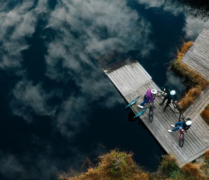 Drei Radfahrer auf einem Steg am See mit Wolkenreflektion im Wasser