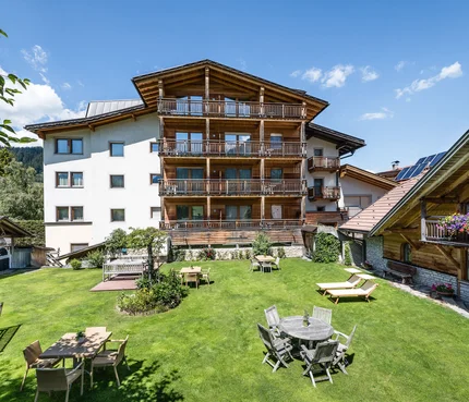 Großer Garten mit Tischen, Stühlen und Liegestühlen vor Alpenhaus