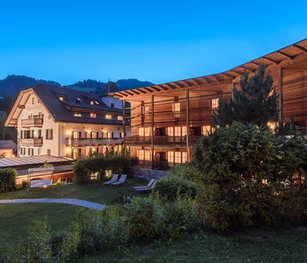 Beleuchtete Hotelgebäude und Garten bei Dämmerung in den Bergen