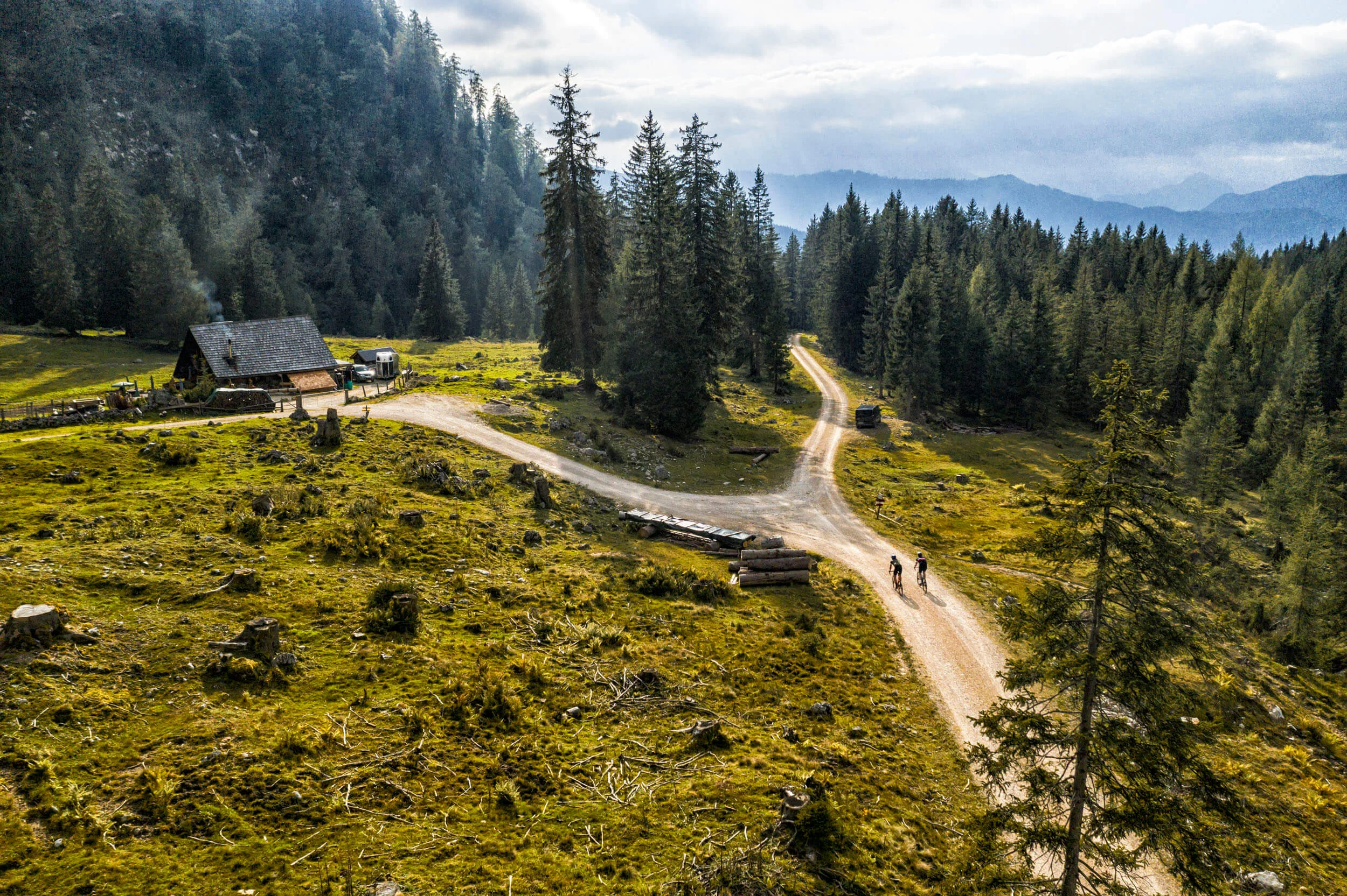 Gravelbike Holidays © WOM Medien GMBH - Andreas Meyer Zwei Radfahrer auf Weg in bewaldeter Berglandschaft mit Hütte