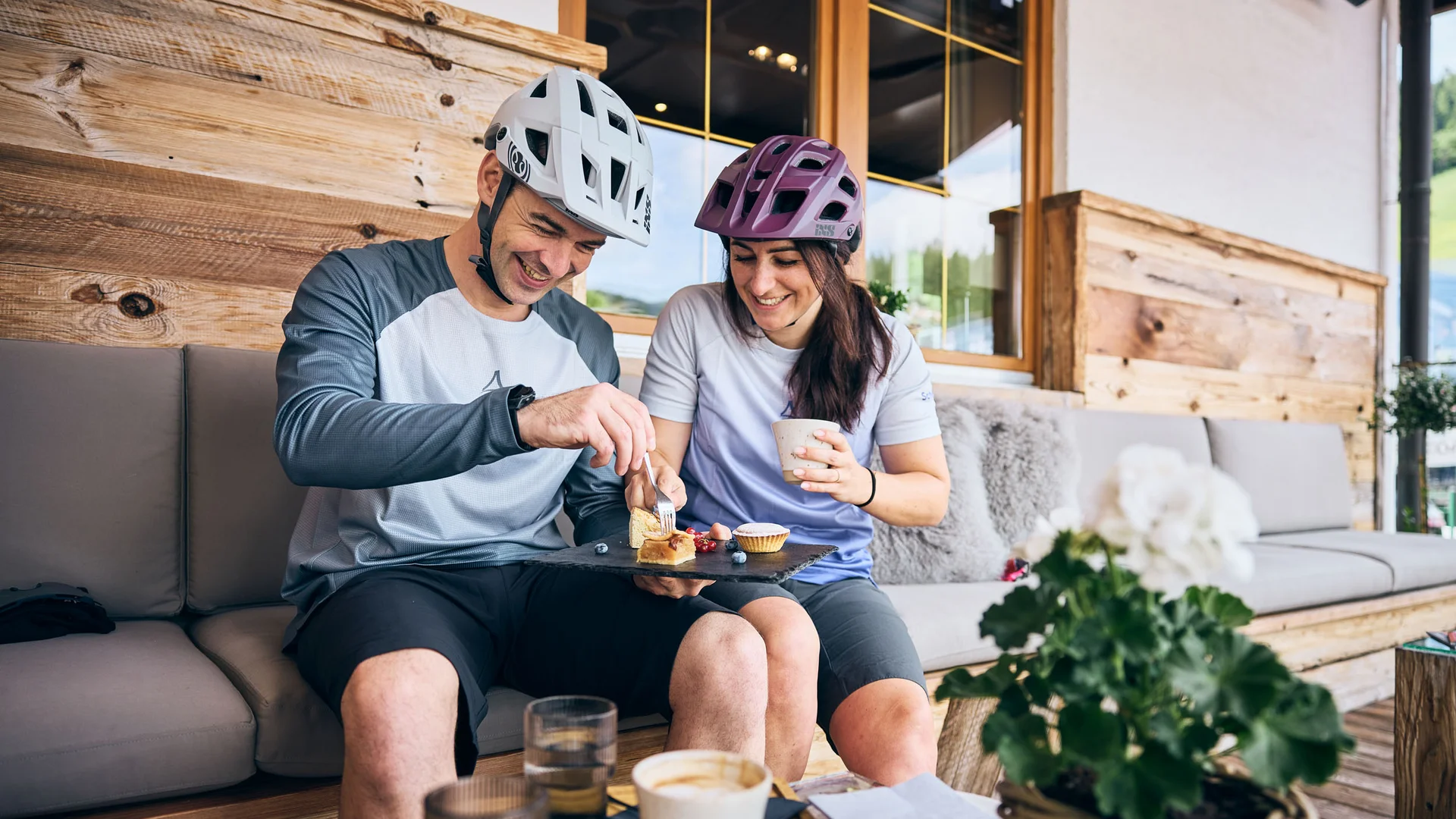 Paar mit Fahrradhelmen teilt Kuchen und Kaffee auf einer Terrasse