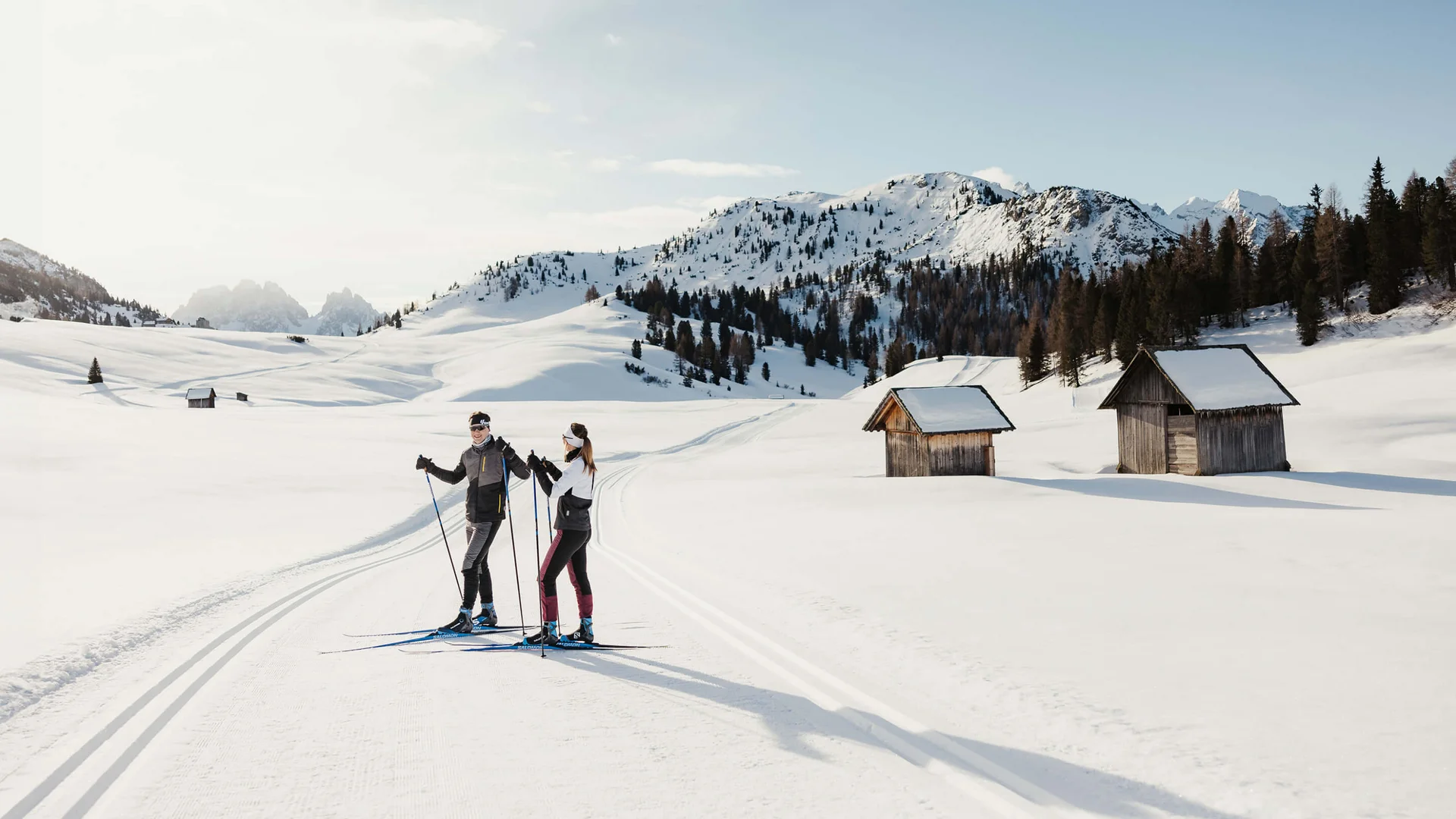 Zwei Skifahrer auf gespurter Loipe in verschneiter Berglandschaft mit Hütten