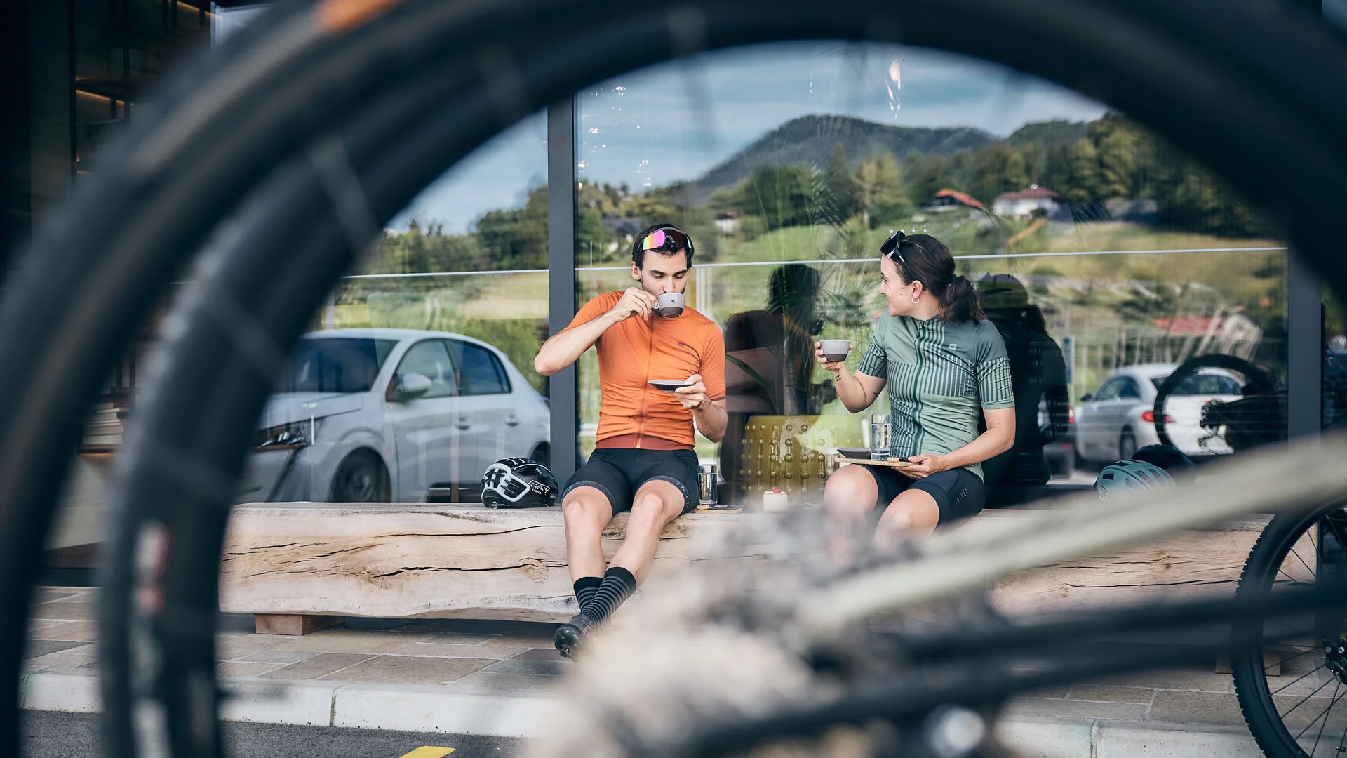 Zwei Radfahrer trinken Kaffee auf Bank, Fahrradreifen im Vordergrund