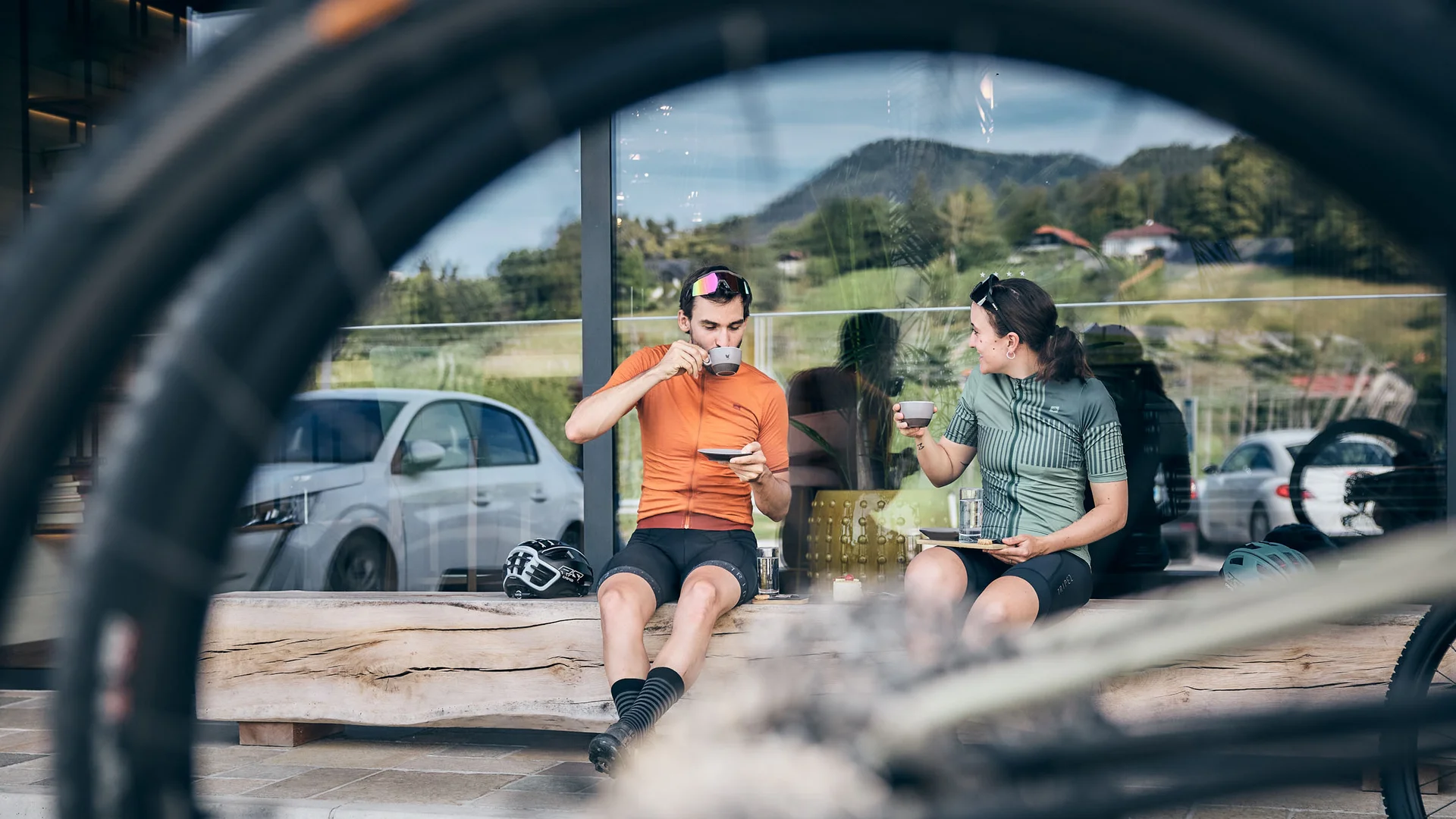 Bikehotel © Tobias Köhler Zwei Radfahrer trinken Kaffee auf Bank, Fahrradreifen im Vordergrund