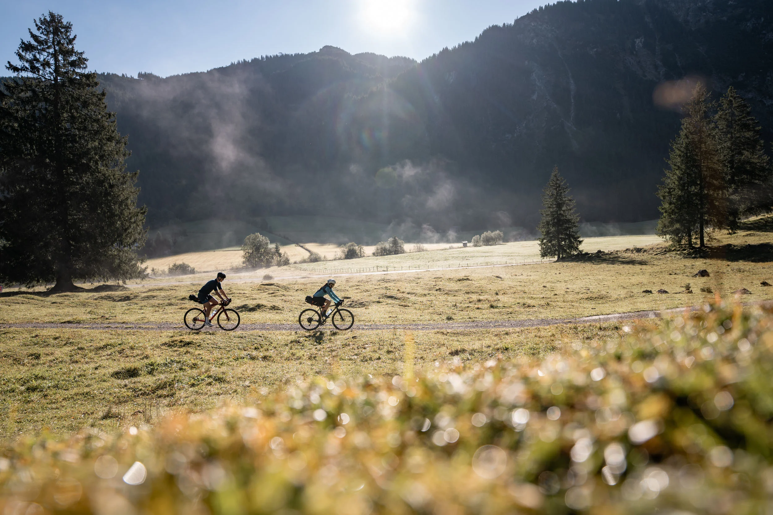 Gravelbike Holidays © Andreas Vigl Zwei Radfahrer fahren auf einem Feldweg in einer bergigen Landschaft bei Sonnenschein