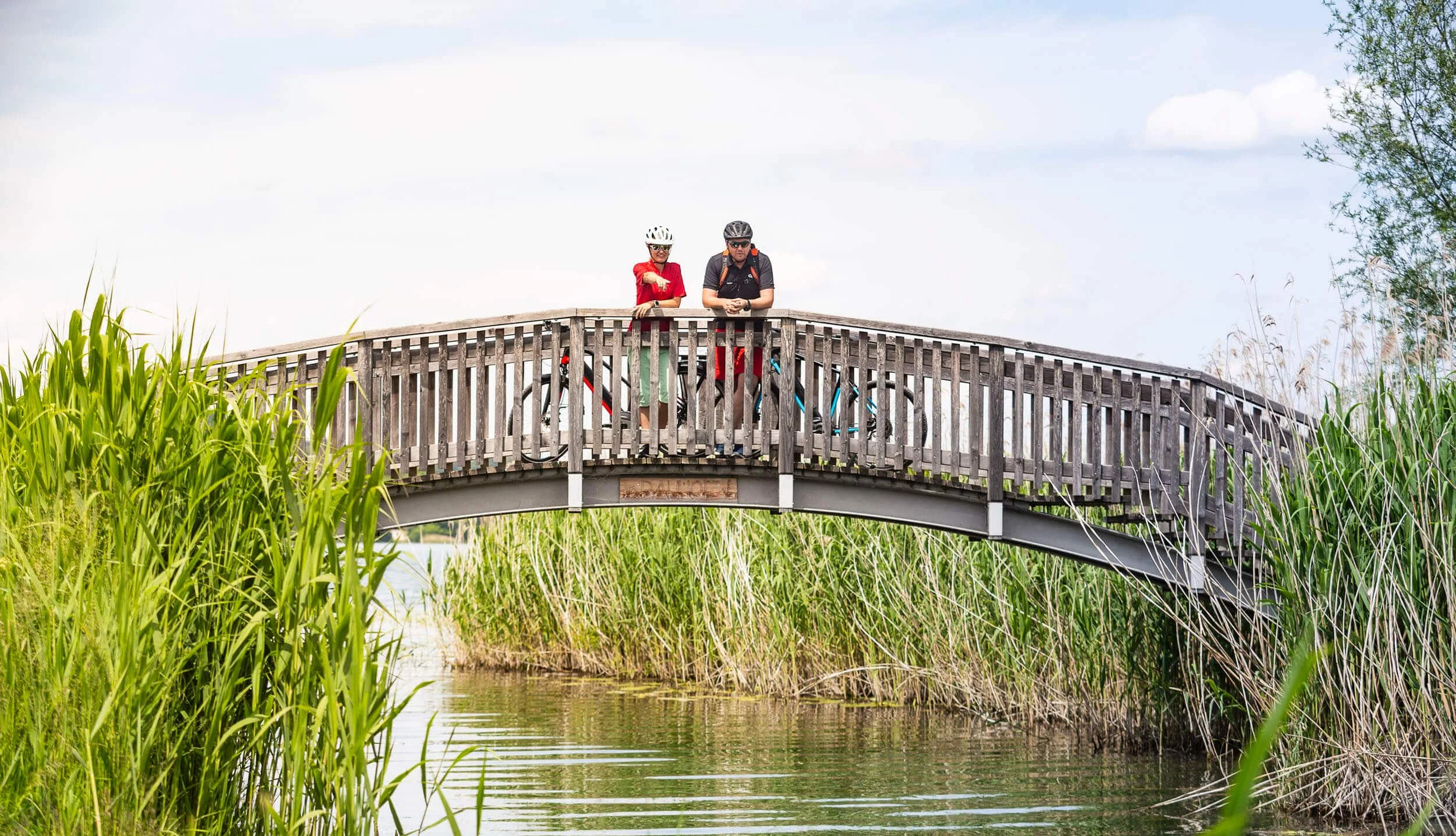 Radhotel © Velontour Zwei Radfahrer auf einer Holzbrücke über einen Fluss mit Schilf