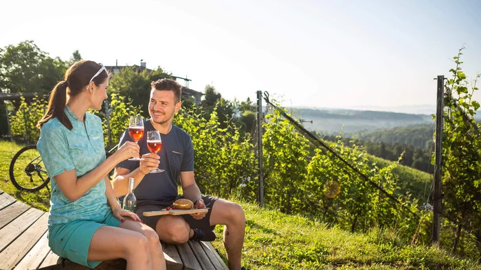 Radhotel © Velontour Paar trinkt Wein und genießt Snack im Weinberg bei Sonnenschein