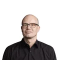 Mann mit Brille und schwarzem Hemd vor weißem Hintergrund