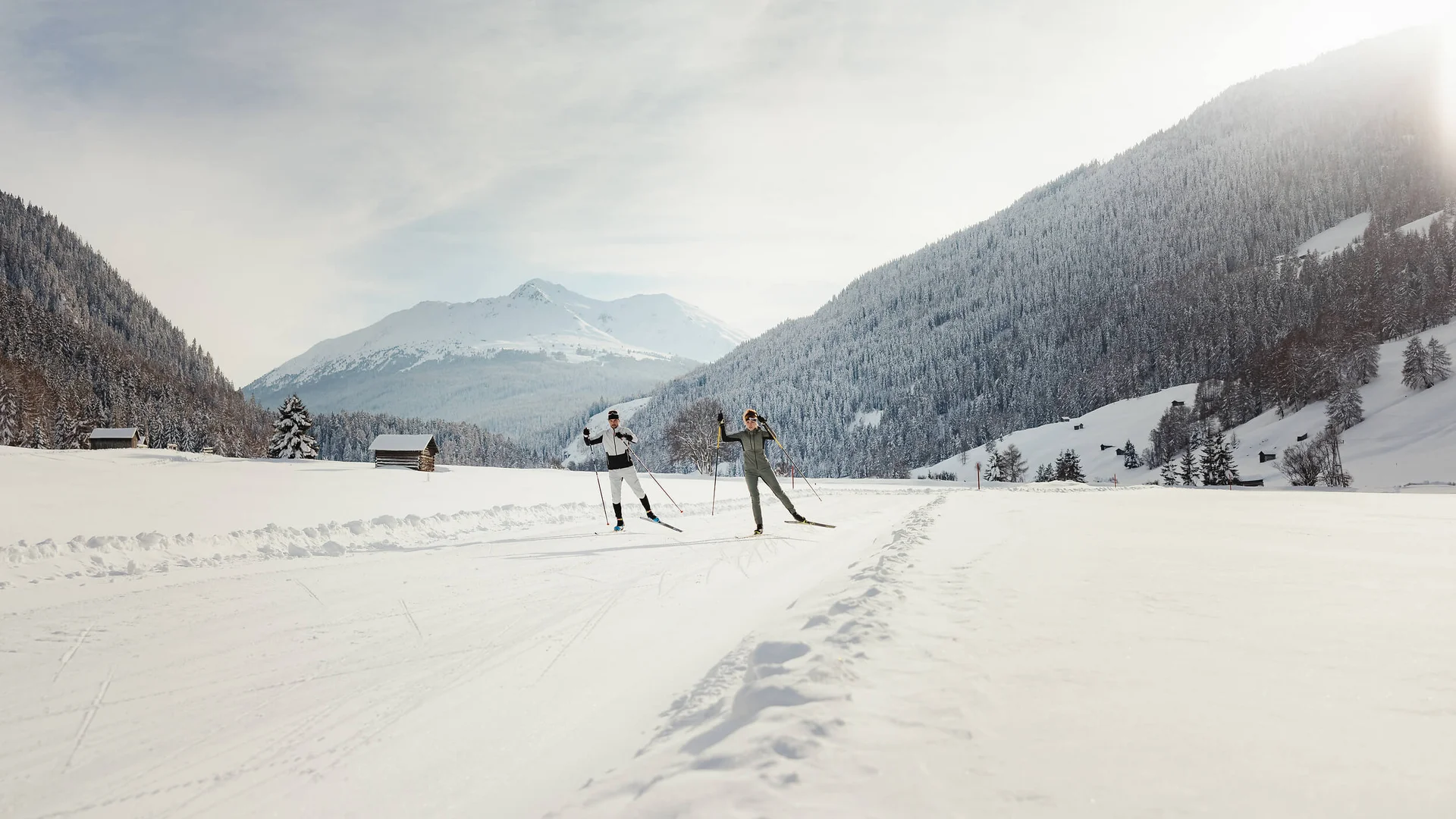 Langlauf & Skitourenhotel © Alex Moling Zwei Langläufer auf verschneiter Strecke vor bewaldeten Bergen bei Sonnenlicht