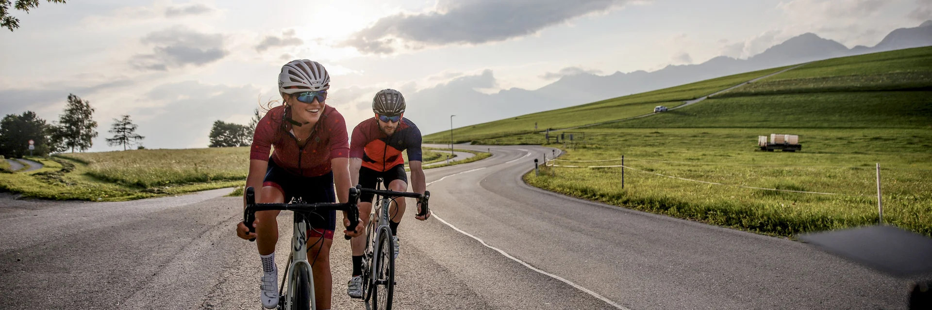 Roadbike Holidays © Felix Saller Zwei Radfahrer fahren auf einer Landstraße bei Sonnenuntergang