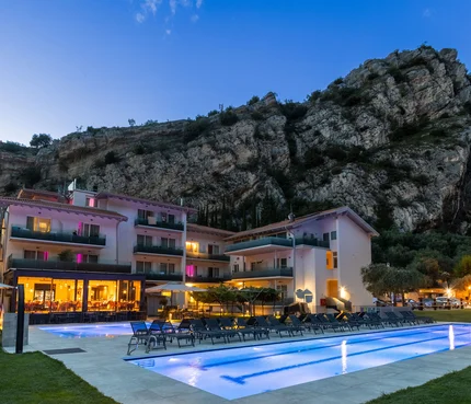 Hotel mit beleuchtetem Pool vor Felsklippe bei Abenddämmerung