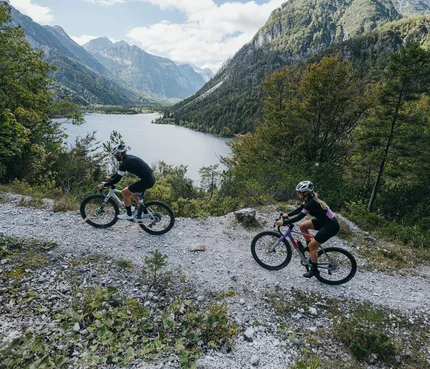 Zwei Radfahrer auf Bergweg mit See und Bergen im Hintergrund