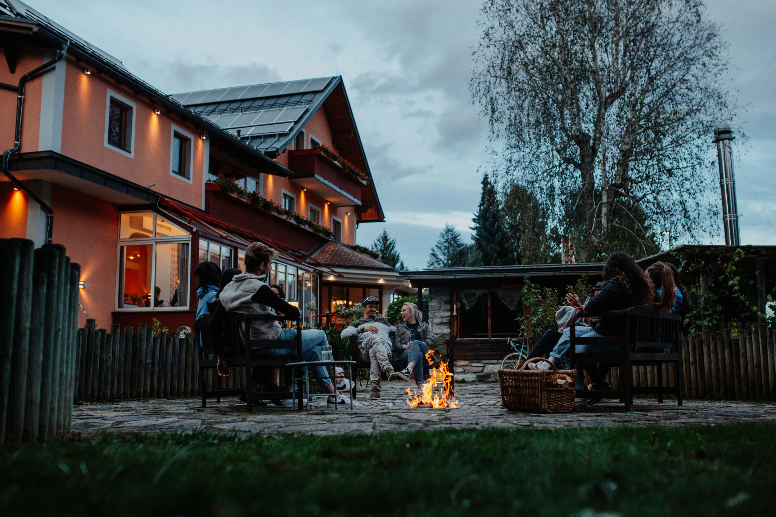 Motorradhotel © Niko Opetnik Gruppe von Menschen sitzt abends um ein Lagerfeuer im Garten eines Hauses