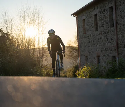 Radfahrer in schwarzer Kleidung fährt auf Landstraße bei Sonnenuntergang
