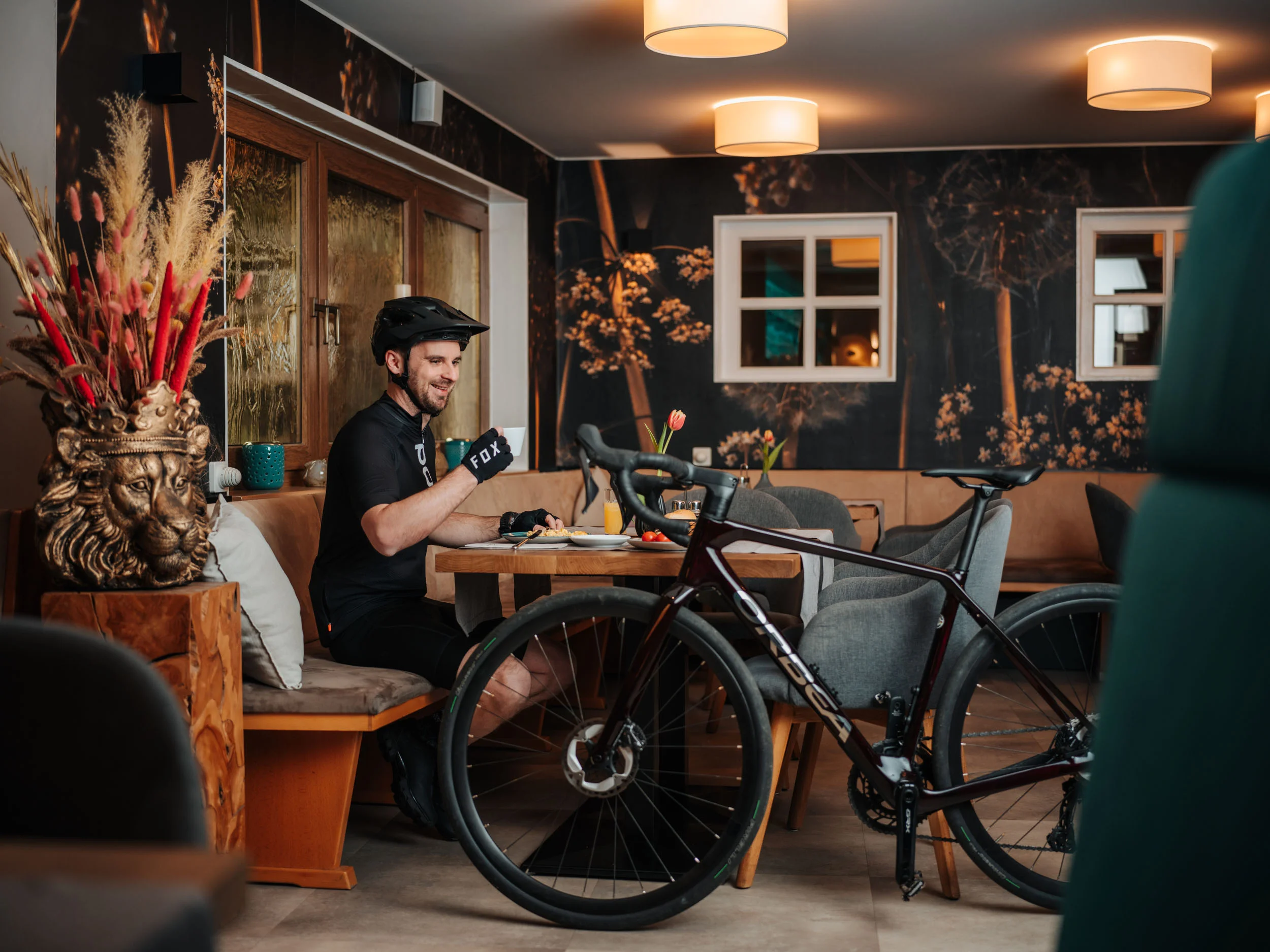 Bikehotel © Martin Hoffmann Radfahrer in schwarzer Ausrüstung trinkt Kaffee neben seinem Fahrrad in Café