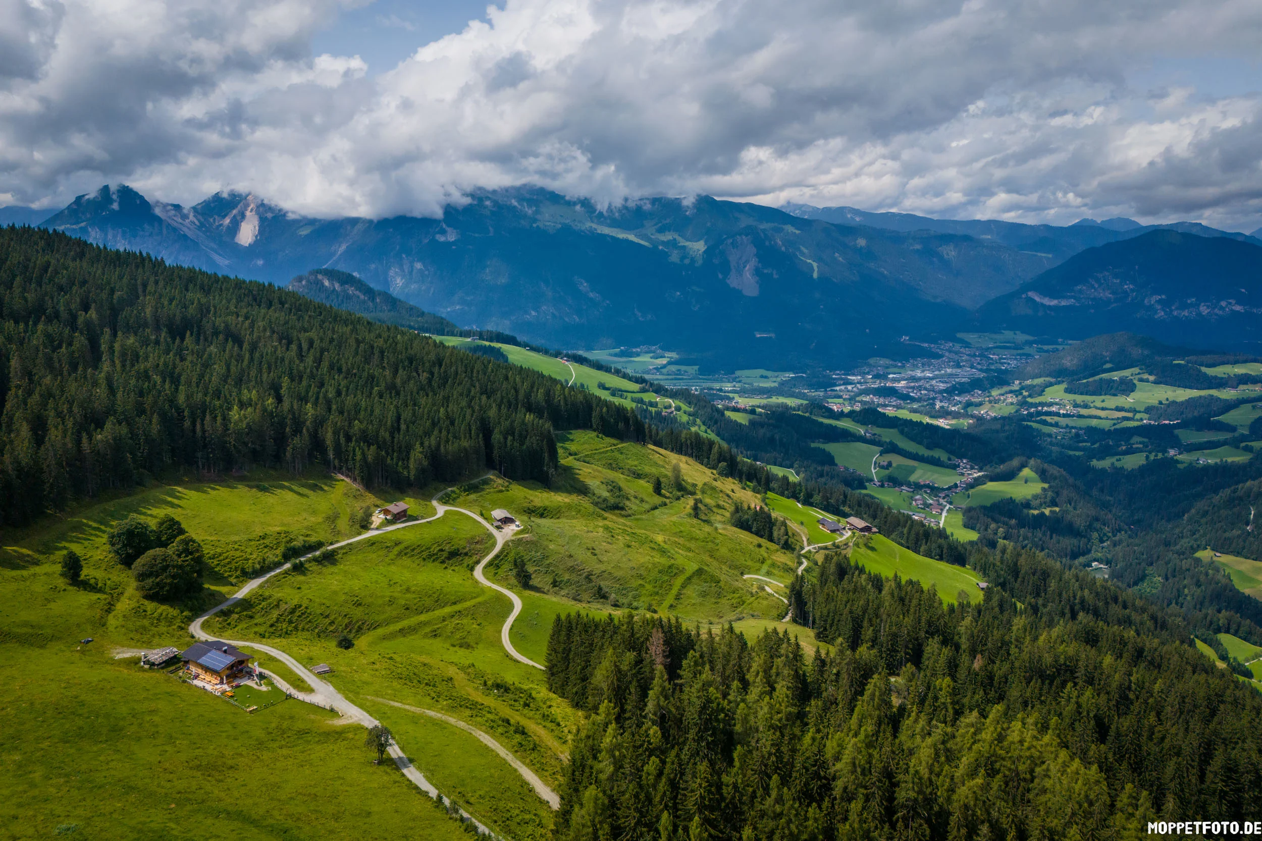 Berglandschaft mit Wäldern, Wiesen und Bergen unter wolkenverhangenem Himmel