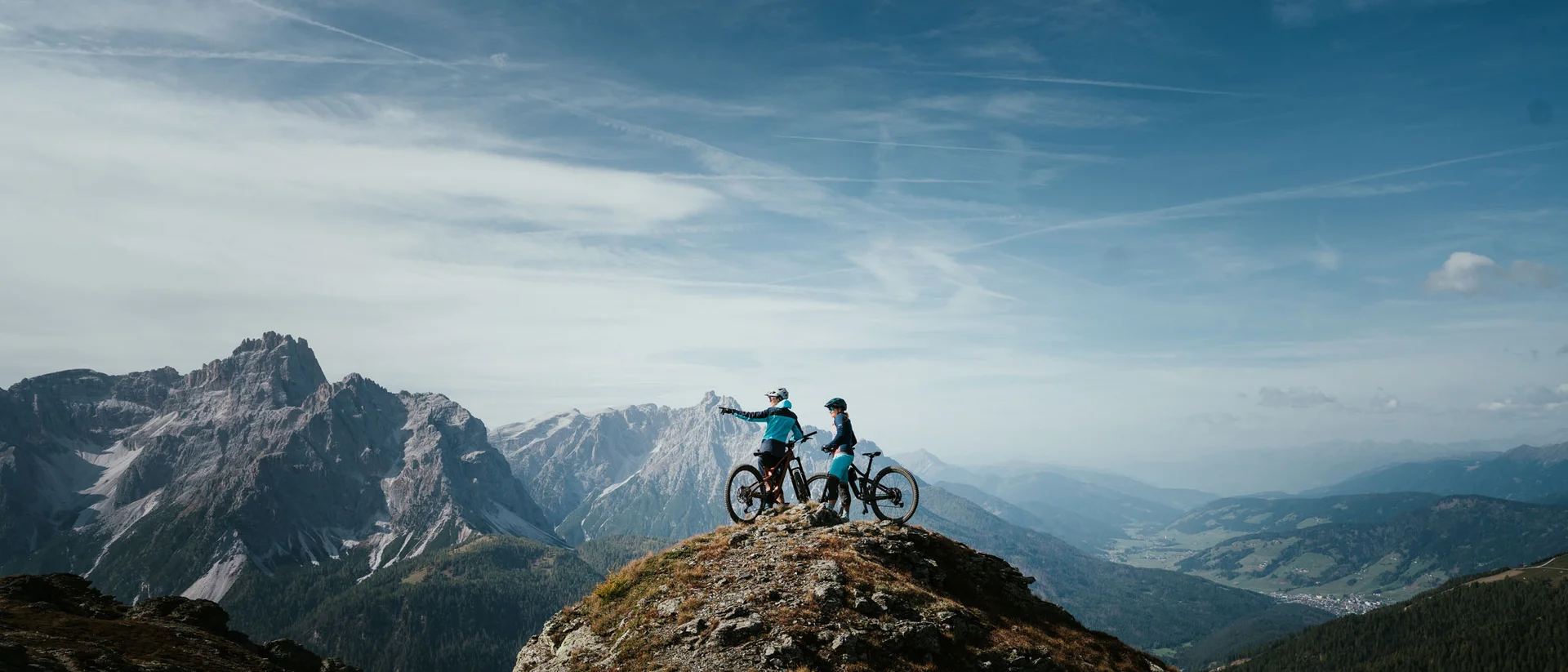 Zwei Mountainbiker auf einem Berggipfel mit Ausblick auf Gebirge