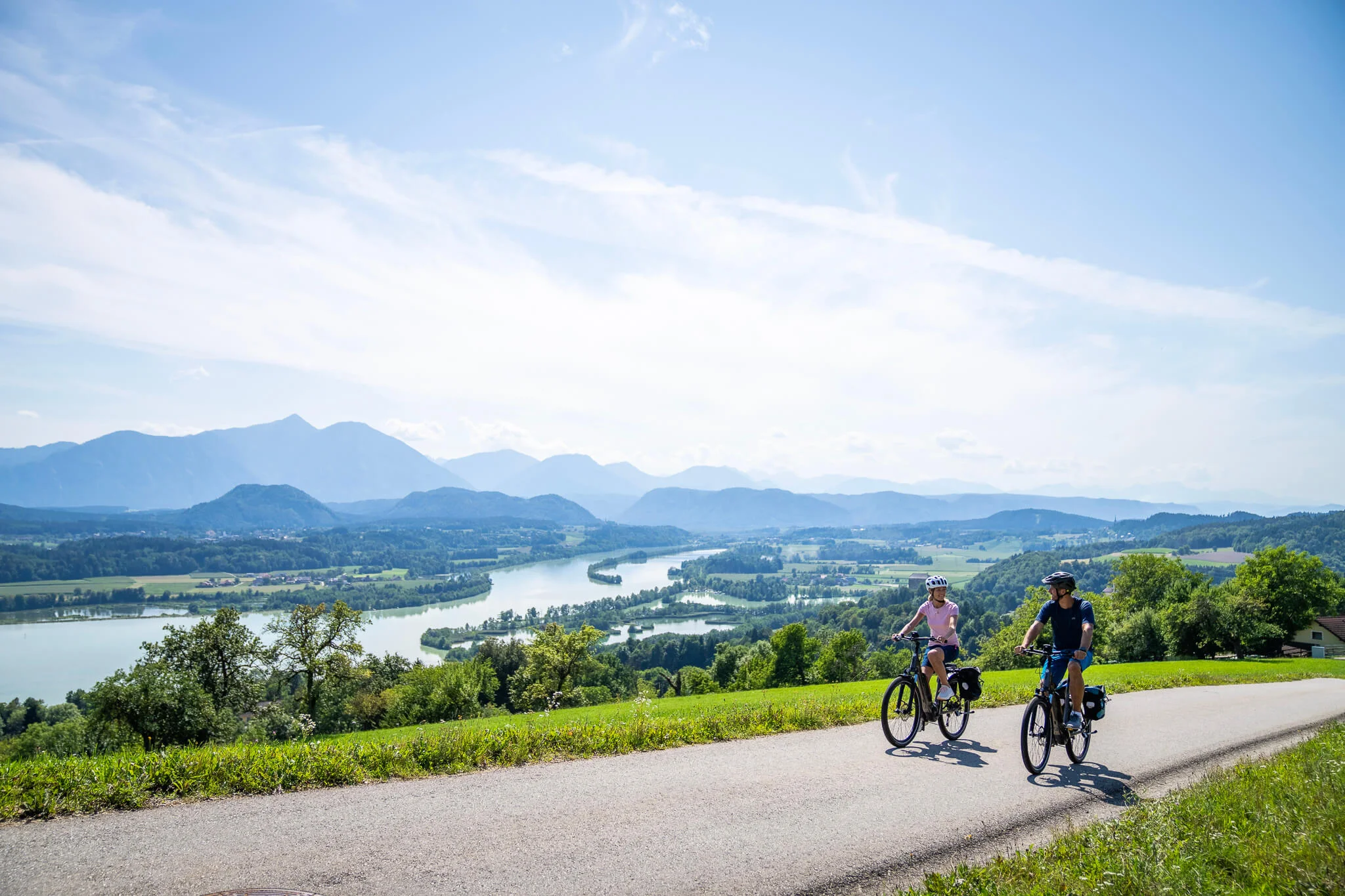 Marken © Kärnten Werbung - Gert Perauer Zwei Radfahrer fahren auf Landstraße mit Alpenblick und Fluss im Tal