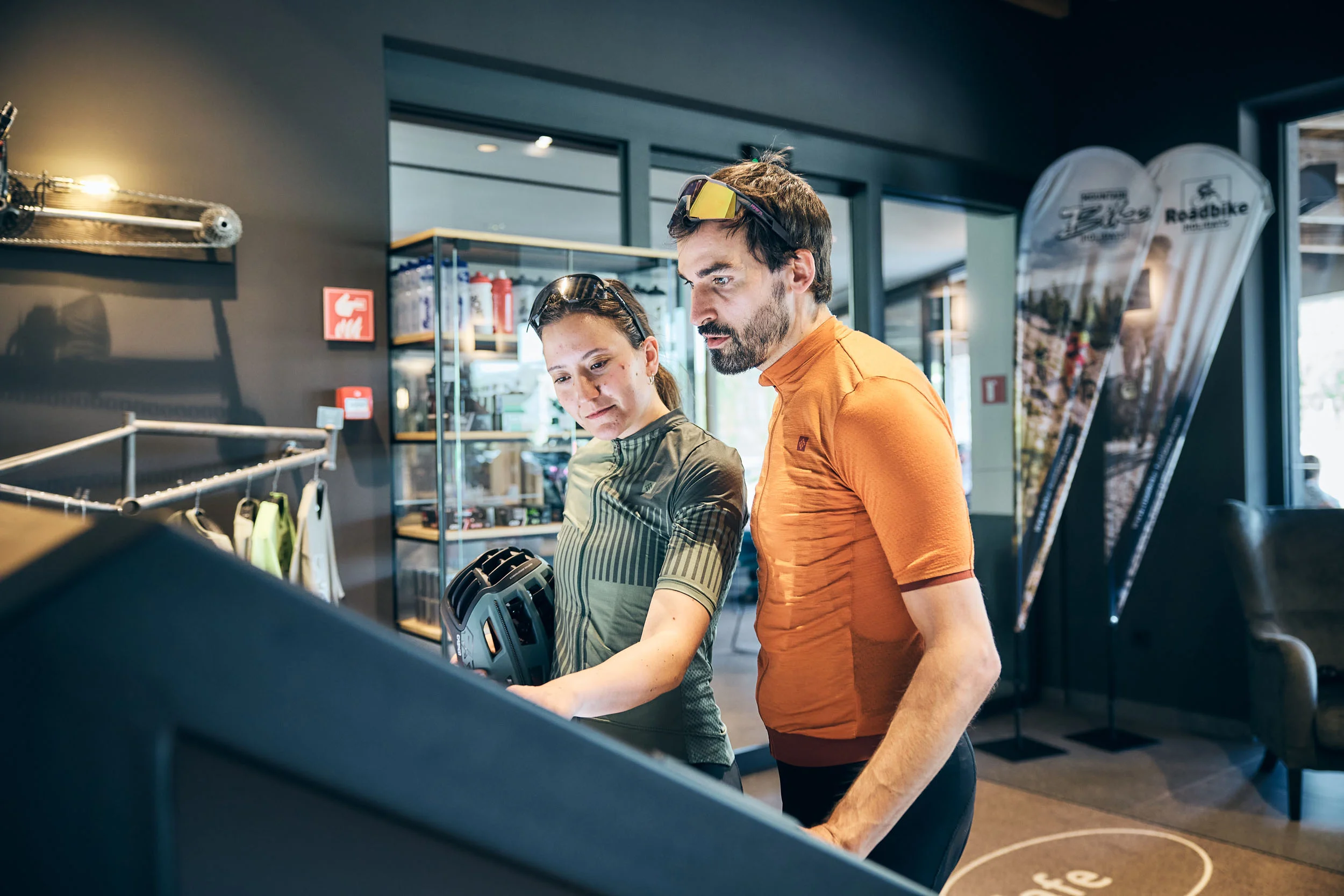 Zwei Radfahrer in Sportkleidung schauen auf einen Bildschirm in einem Geschäft
