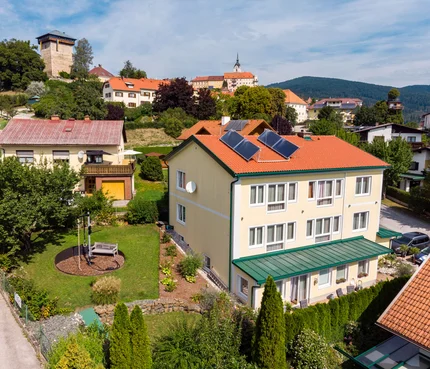 Dorf mit Häusern, Solarpanelen und Burgturm im Hintergrund bei klarem Himmel