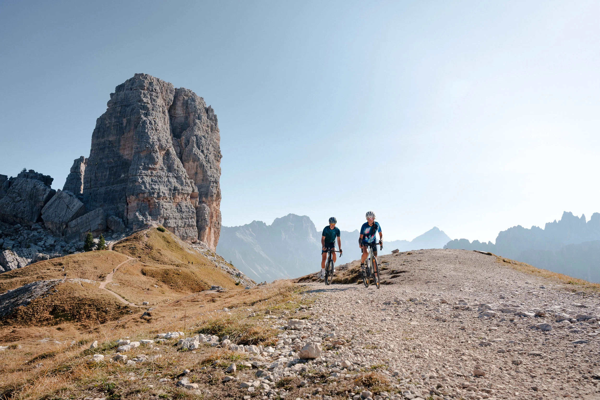 Gravelbike Holidays © Josef Plaickner Zwei Radfahrer auf Bergweg mit großem Felsen und Bergkulisse im Hintergrund