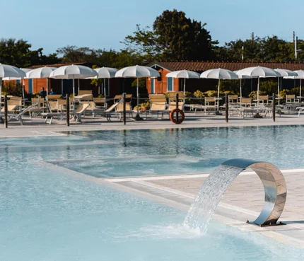 Moderner Pool mit Wasserfontäne und Liegestühlen unter weißen Sonnenschirmen