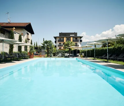 Großer Pool mit Liegestühlen und Sonnenschirmen vor einem modernen Gebäude