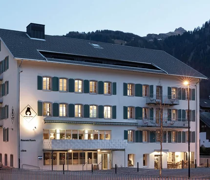 Hotelgebäude mit beleuchteten Fenstern am Abend in bergiger Umgebung