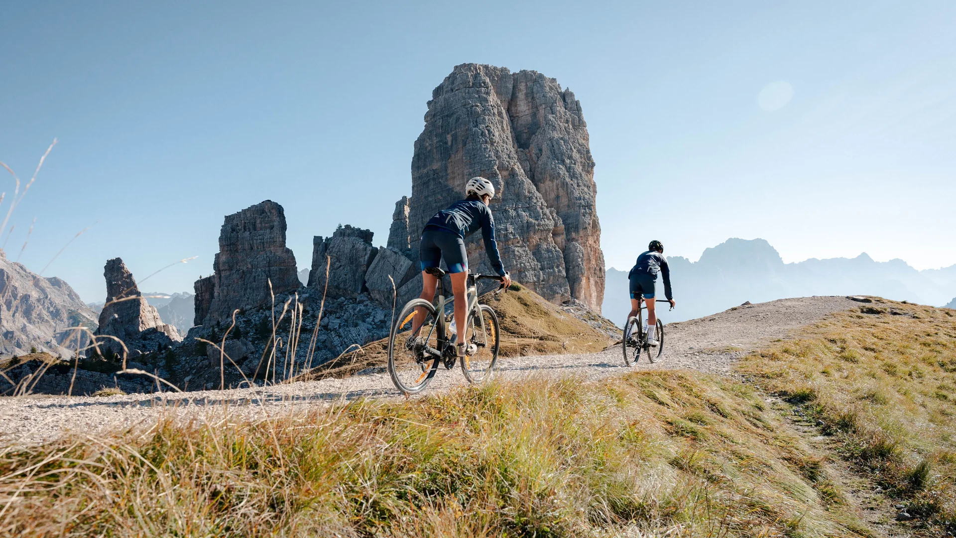 Bikehotel © Josef Plaickner Zwei Radfahrer fahren auf einem Bergweg vor großer Felsformation im Sonnenschein