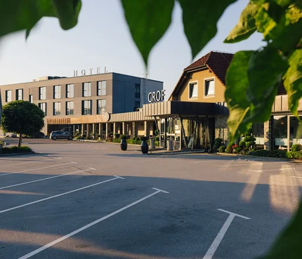 Hotelgebäude mit Parkplatz, teilweise eingerahmt von grünen Blättern bei Sonnenuntergang
