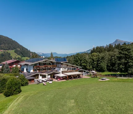 Berghotel mit Solarpanels umgeben von Wiesen und Bergen bei klarem Himmel