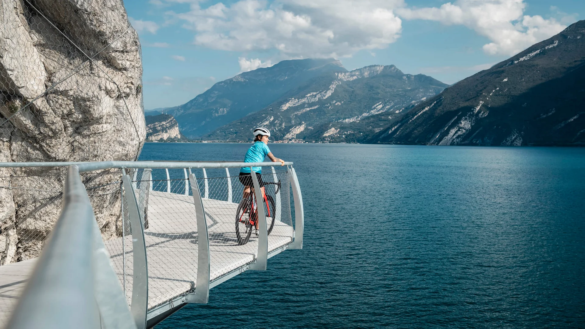 Roadbike Holidays © Alex Moling Radfahrer auf Steg mit Blick auf See und Berge bei sonnigem Wetter