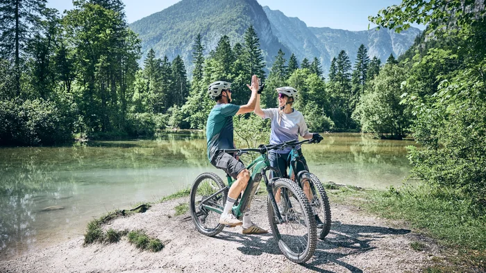 Zwei Radfahrer geben sich am See in den Bergen ein Highfive