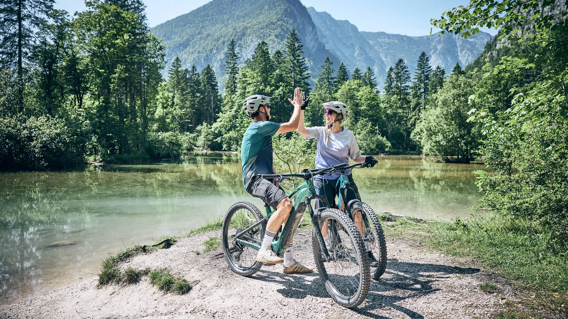 Zwei Radfahrer geben sich am See in den Bergen ein Highfive