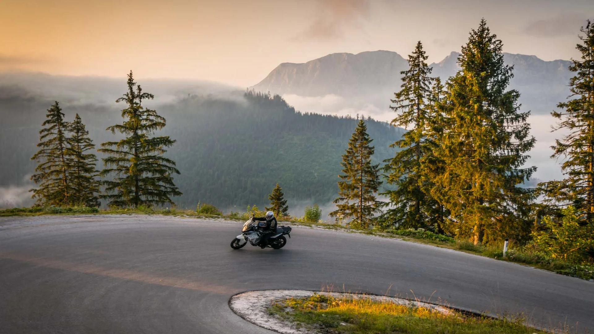 Motorradfahrer auf kurviger Bergstraße bei Sonnenaufgang
