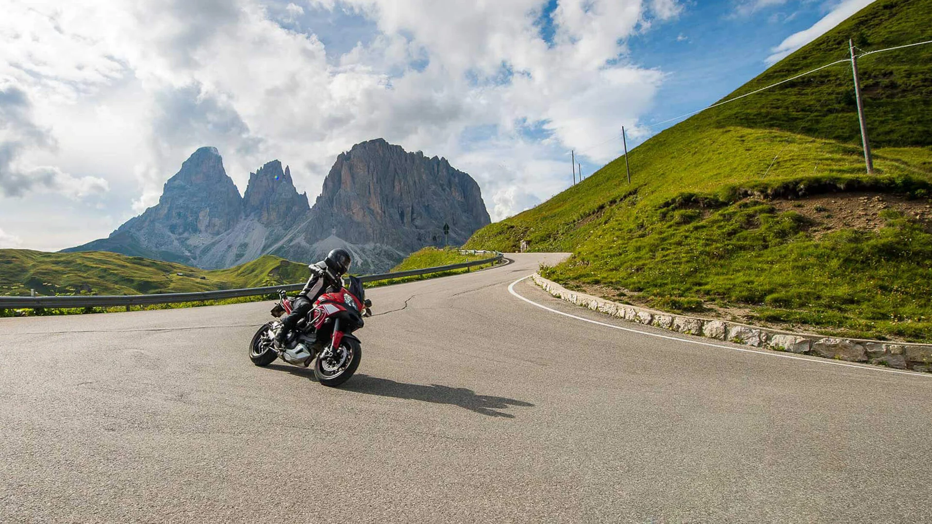 Motorradhotel © Arik Oberrauch Motorradfahrer auf Bergstraße mit Felsen und bewölktem Himmel