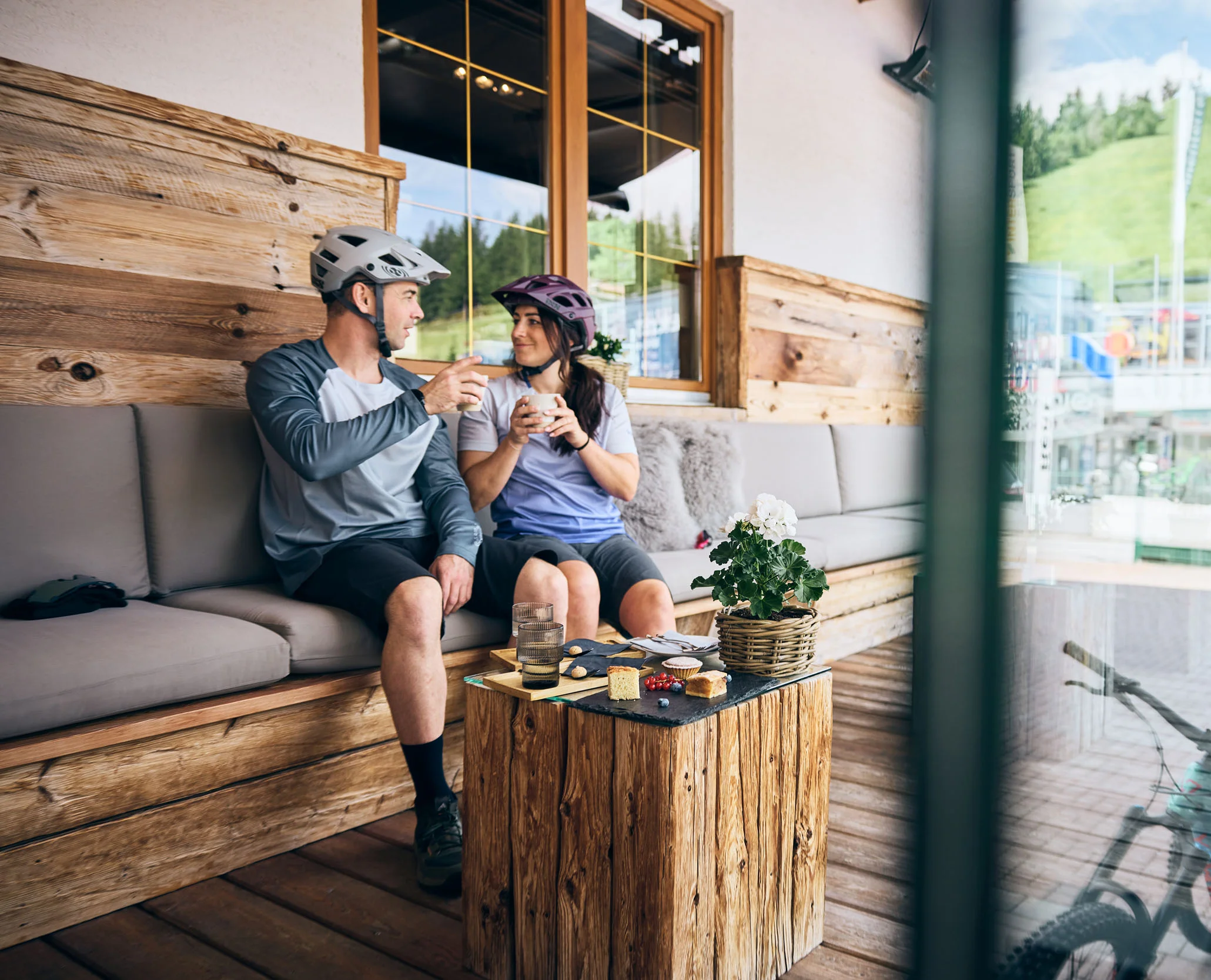 Mountain Bike Holidays © Tobias Köhler Paar mit Fahrradhelmen trinkt Kaffee in rustikalem Café mit Mountainbikes draußen
