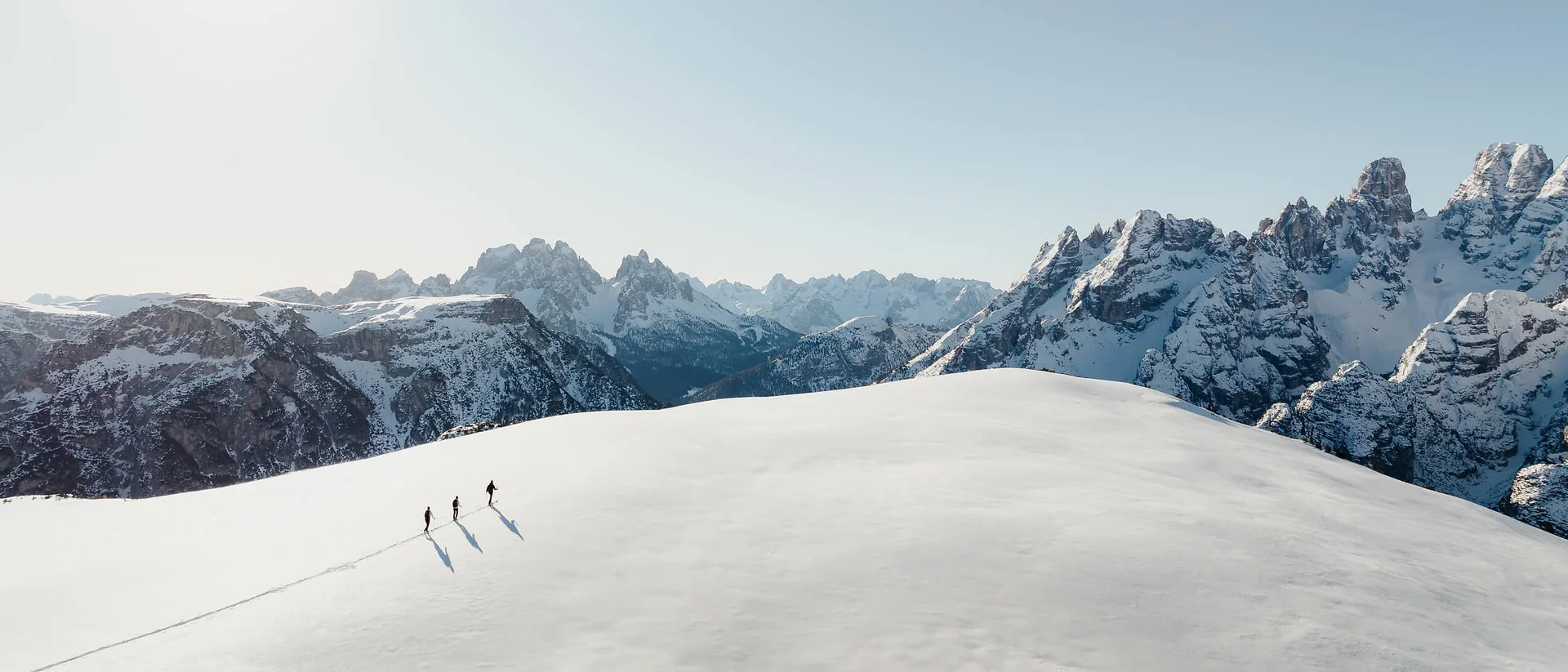 Drei Wanderer gehen auf einem schneebedeckten Berg mit Bergen im Hintergrund