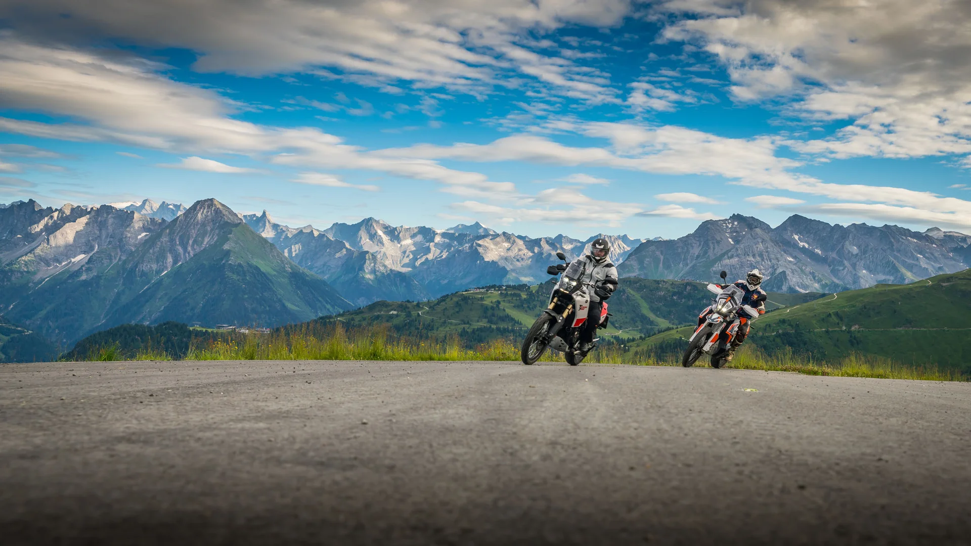 MoHo - Motorrad Hotels © Moppetfoto.de Zwei Motorradfahrer auf Bergstraße vor Alpenlandschaft unter bewölktem Himmel