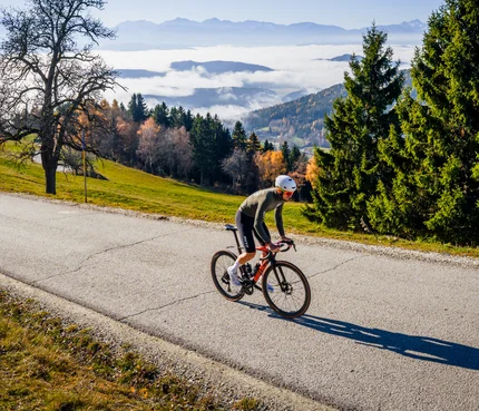Radfahrer fährt auf Bergstraße bei sonnigem Herbstwetter mit Nebel im Tal