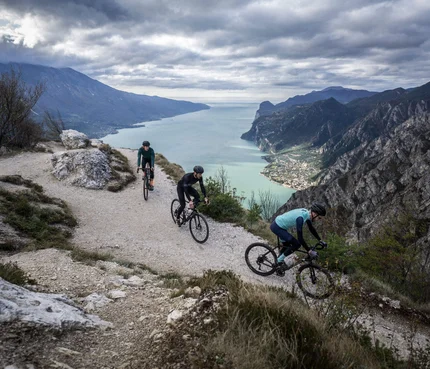 Drei Radfahrer auf einem Bergweg mit Blick auf einen See und Berge