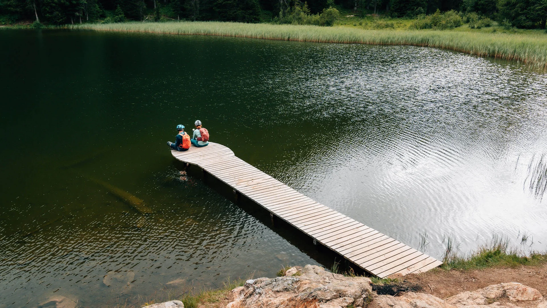 Zwei Radfahrer sitzen auf einem Steg über einem See in der Natur