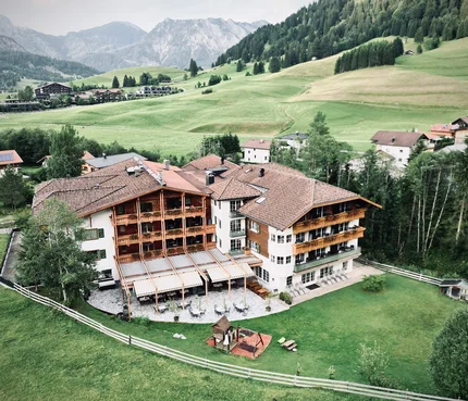 Blick auf ein Hotel im Bergtal mit grünen Wiesen und Bergen im Hintergrund