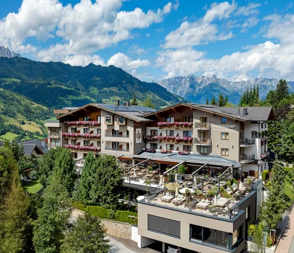 Hotel Alpendorf mit Terrasse in bergiger Landschaft bei Sonnenschein
